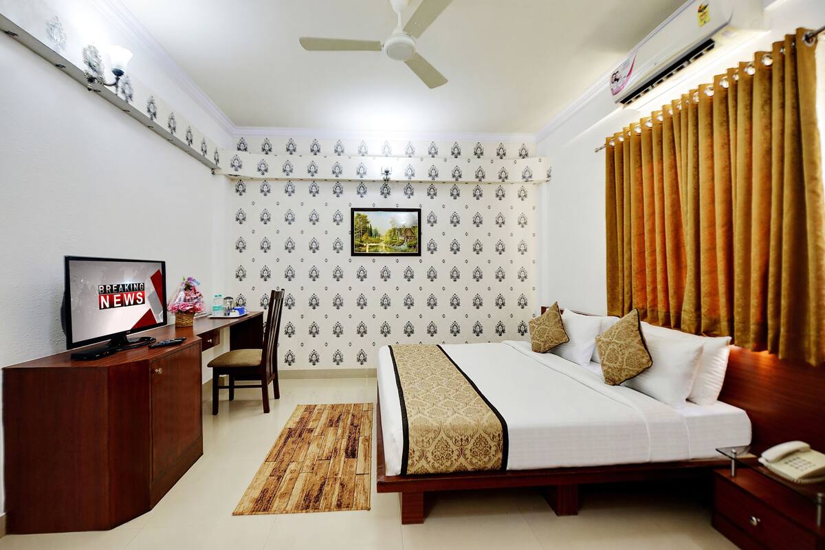 A hotel room with a bed, a desk, a chair, a television, and a window with curtains.