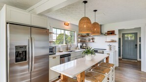 A modern kitchen with a stainless steel refrigerator, a central island with bar stools, and a large window providing natural light. - Boat Dock + Covered Patio: Cherokee Lake Escape! (Mooresburg)