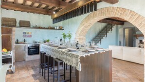 A kitchen with a central island, a built-in oven, and a stone archway leading to a staircase. - Le Residenze dei Potti 12 (Todi)