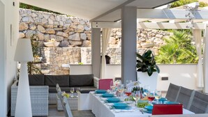 Un espace repas agrémenté d’un mur en pierre, de sièges en plein air et d’une table dressée pour un repas.