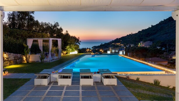 Une piscine avec des chaises longues, une pergola et une vue sur la mer au crépuscule.