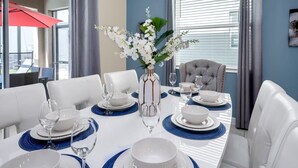 A dining area with a white table set for six, blue placemats, white plates, and clear glassware. A vase with white flowers is centered on the table. - Minions, Star Wars & Frozen Rooms! With Game Room (Kissimmee)