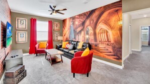 A living room with a large mural, a black leather sofa, red chairs, and a ceiling fan. - Minions, Star Wars & Frozen Rooms! With Game Room (Kissimmee)