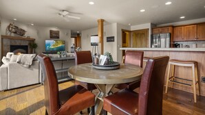 Un salon moderne avec une table ronde en bois, des fauteuils en cuir, un téléviseur à écran plat et une cheminée.