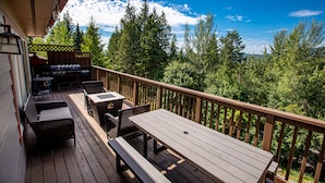Une terrasse en bois avec une table et des bancs, entourée d’une balustrade en bois et d’une forêt dense.