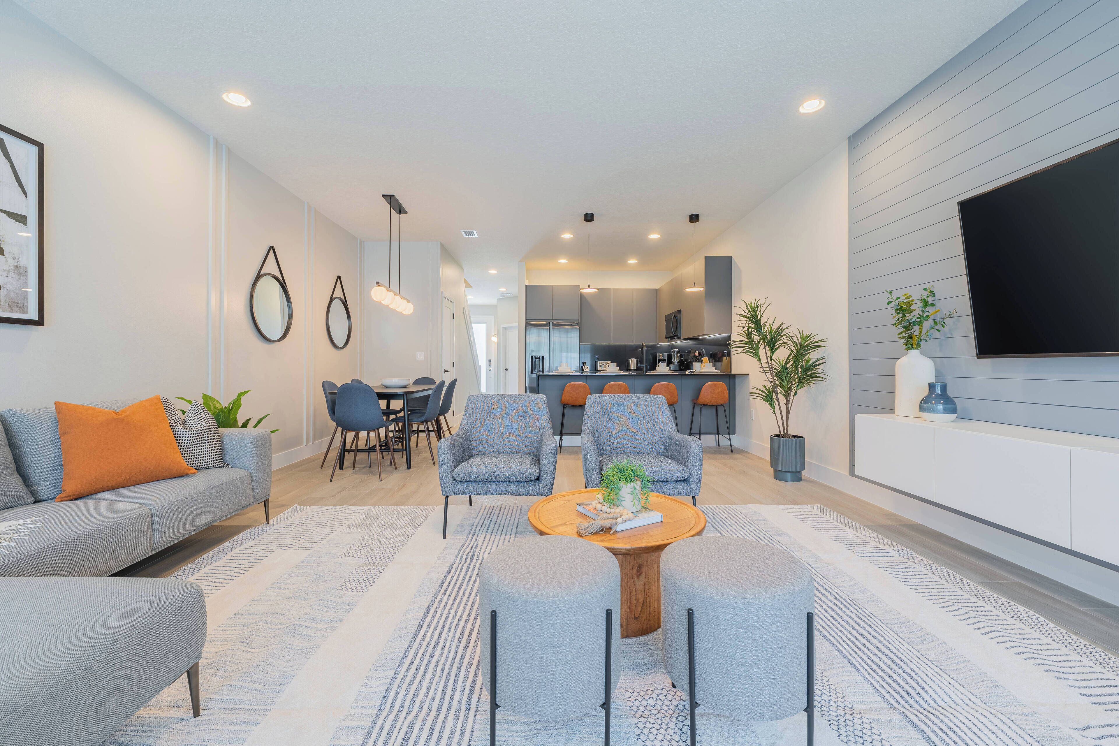 A modern living room with a grey sofa, two armchairs, a coffee table, and a dining area with a table and chairs.