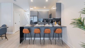 A modern kitchen with a central island, bar stools, and a dining area with a table and chairs. - Your Orlando Retreat: Warm and Welcoming Townhome (Clermont)