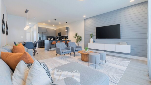 A modern living room with a sofa, armchairs, a coffee table, and a TV mounted on the wall. - Your Orlando Retreat: Warm and Welcoming Townhome (Clermont)