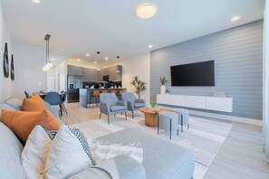 A modern living room with a sofa, armchairs, a coffee table, and a TV mounted on the wall. - Your Orlando Retreat: Warm and Welcoming Townhome (Clermont)