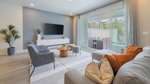 A modern living room with a flat-screen TV, grey sofas, a coffee table, and a large sliding glass door leading to an outdoor area. - Your Orlando Retreat: Warm and Welcoming Townhome (Clermont)