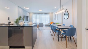 A modern kitchen with a central island, a dining area with blue chairs, and a living space with a sofa and TV. - Your Orlando Retreat: Warm and Welcoming Townhome (Clermont)