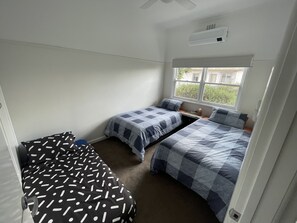 A small, clean room with two single beds, a window with blinds, and a ceiling fan. - Central Murtoa Home with Lake view, family friendly. (Murtoa)