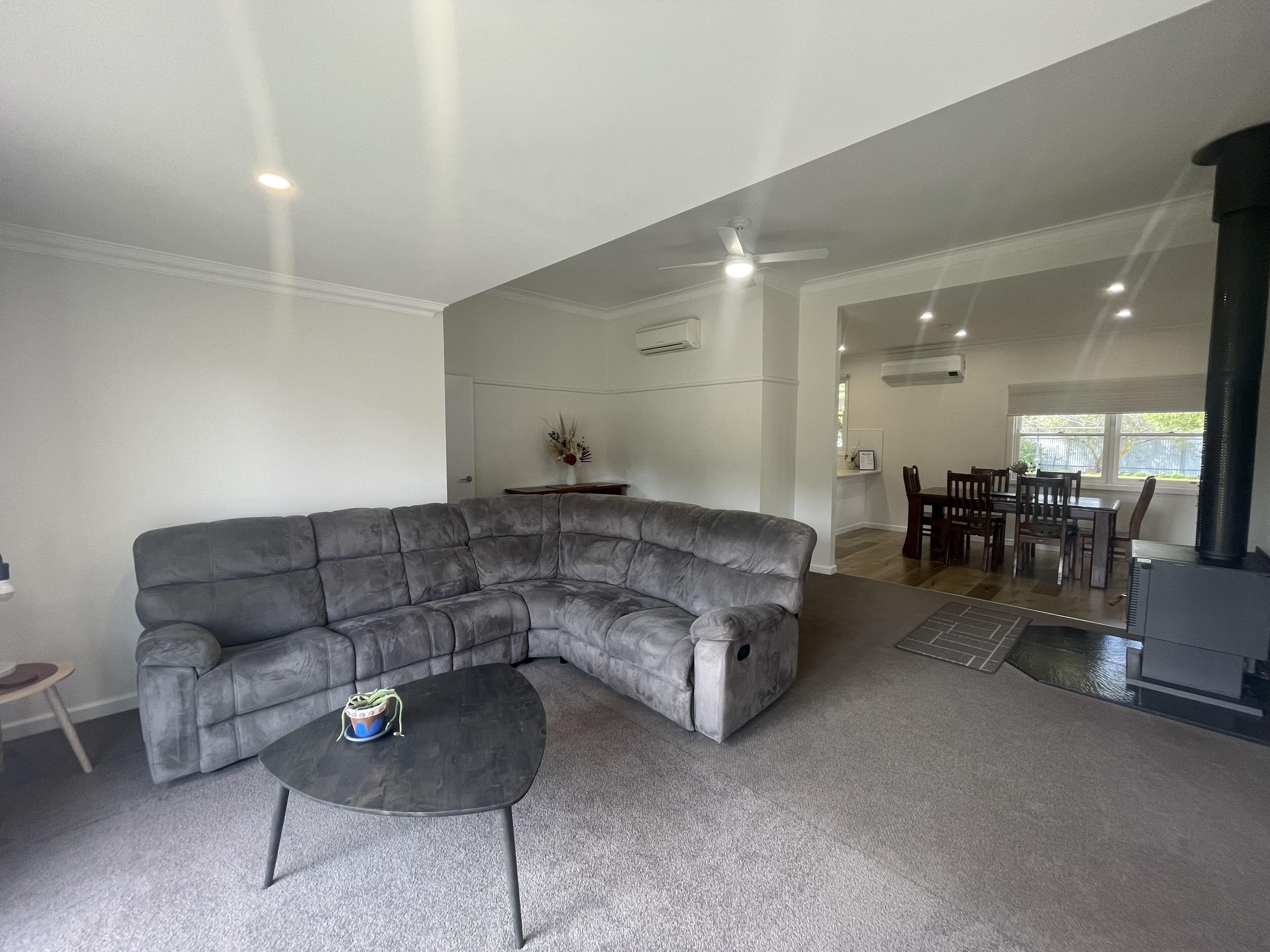 A spacious living room with a large grey sectional sofa, a small round coffee table, and a dining area in the background.
