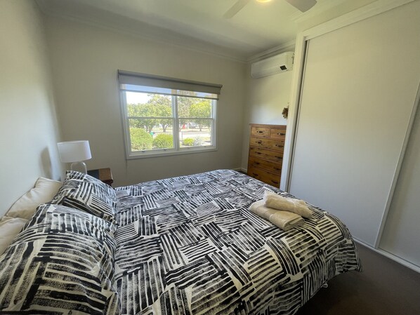 Ein Schlafzimmer mit einem Bett, einem Schminktisch, einem Fenster und einem Deckenventilator.