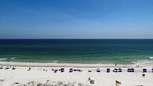 Une plage bordée de rangées de parasols et de chaises longues, un ciel dégagé et l’océan.