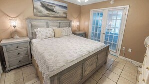 Une chambre à coucher avec un lit, des tables de chevet, un ventilateur de plafond, un tableau et une porte avec des stores.
