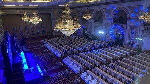 A large hall with rows of tables and chairs, ornate chandeliers, and a stage with speakers. - GRAND EMPIRE PALACE HOTEL (Surabaya)