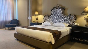 A large bed with a headboard, two bedside tables with lamps, a chair, and a curtain. - GRAND EMPIRE PALACE HOTEL (Surabaya)