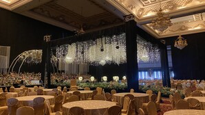 A banquet hall with round tables and chairs, a stage with floral arrangements, and ornate chandeliers. - GRAND EMPIRE PALACE HOTEL (Surabaya)