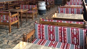 A rustic dining area with wooden tables and benches, a stone floor, and a high ceiling with exposed beams.