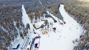 An aerial view of a snow-covered resort with ski slopes, cabins, and a central building.
