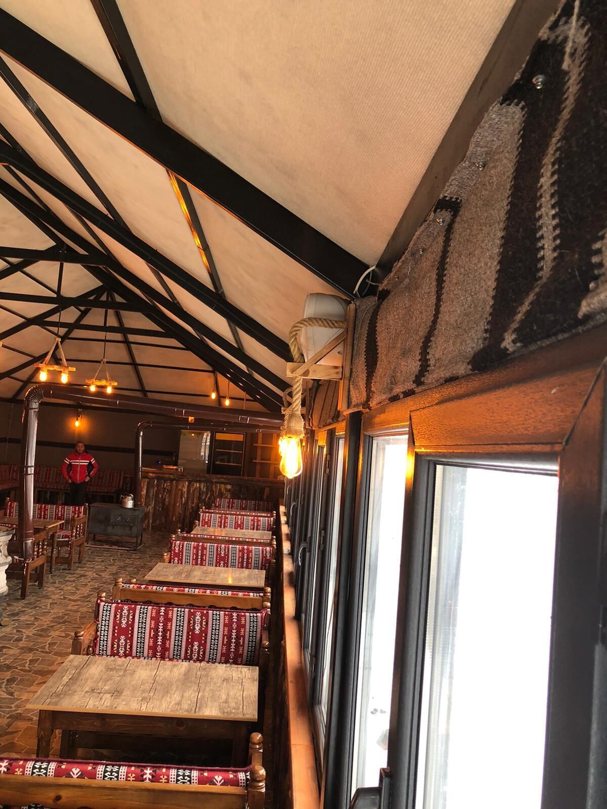 Ein rustikales Interieur mit Holzbänken, einer hohen Decke mit freiliegenden Balken und einem großen Fenster, das natürliches Licht hereinlässt.