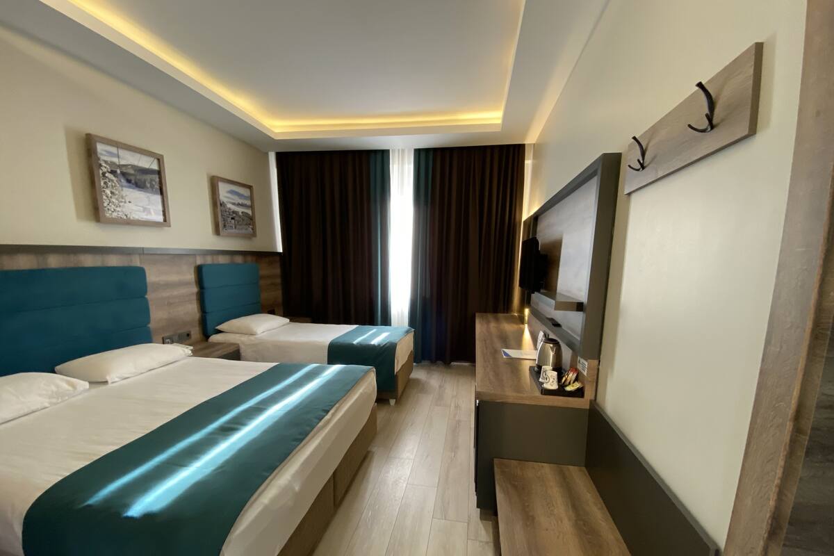 Habitación de hotel con dos camas, un escritorio, un televisor y una ventana con cortinas.