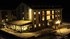 A snow-covered building with a large glass enclosure and a covered outdoor area, illuminated by interior lights.