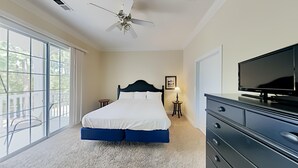 Un dormitorio con una cama, ventilador de techo, televisor y un ventanal grande.