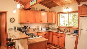 A kitchen with wooden cabinets, a gas stove, a sink, and a window. - Cute, spacious rainforest cottage close to HVNP (Volcano)