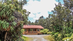 A house with a gravel driveway, surrounded by dense greenery and trees. - Cute, spacious rainforest cottage close to HVNP (Volcano)