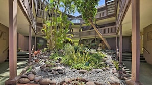 A multi-level atrium with a central garden area featuring rocks, plants, and a wooden walkway. - Gorgeous Oceanfront Kihei Condo w/ Balcony! (Kihei)