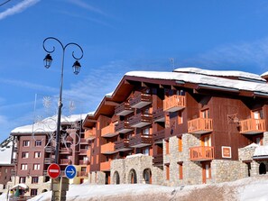 Um edifício de madeira com várias andares, varandas, paredes de pedra e um telhado coberto de neve.
