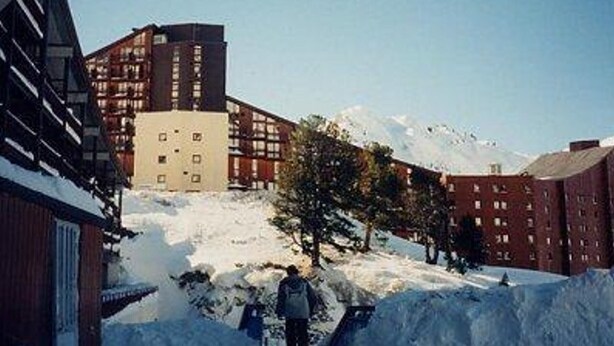 Ein schneebedeckter Berg, im Hintergrund sind Gebäude zu sehen.