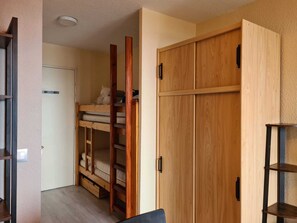 Una habitación con una cama individual superpuesta, un armario de madera y una pequeña mesa.