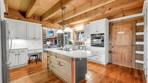 Une cuisine spacieuse avec des meubles blancs, un îlot central et un plafond en bois.