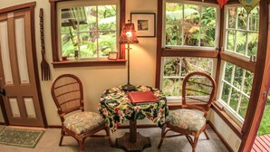 Une pièce d’angle avec une table, deux chaises, une lampe et une fenêtre donnant sur un paysage verdoyant.