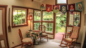 Une pièce avec une baie vitrée, une table à manger avec des chaises, un fauteuil à bascule et une petite table avec une lampe.