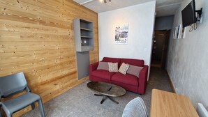 A modern living room with a red sofa, a grey armchair, and a wooden wall.