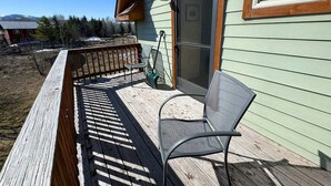 Eine Holzterrasse mit einem Metallstuhl, einer Schlauchaufrolle und einer Schiebetür.