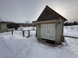 A small, single-story structure with a gabled roof and a white door with a glass panel.