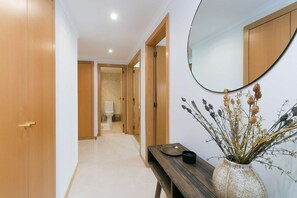 Enter a serene hallway with a door to a bathroom and a cozy bench with a vase of dried plants.