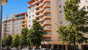 Un edificio residencial de varios pisos con balcones, coches aparcados y árboles.