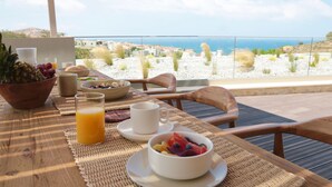 Ein Esstisch mit Obst, einem Glas Orangensaft und Blick auf Meer und Hügel.