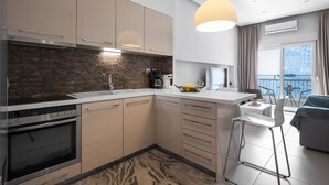 A modern kitchen with a built-in oven, a coffee machine, and a dining area with a view of the sea. - Awesome Sea View Nilie Hospitality MGMT (Thessaloniki)