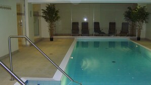 Ein Hallenbad mit klarem Wasser, einer Metallleiter und mehreren Liegestühlen.