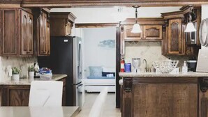 Una cocina con armarios de madera, una isla central y una zona de comedor con mesa y sillas blancas.