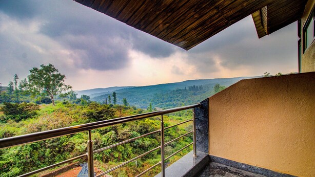A balcony with a metal railing overlooking a lush landscape with trees and hills. - Hirkani Garden & Resort (Mahabaleshwar)