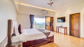 A bedroom with a wooden bed, a small table, an air conditioning unit, a ceiling fan, and a TV on the wall. - Hirkani Garden & Resort (Mahabaleshwar)