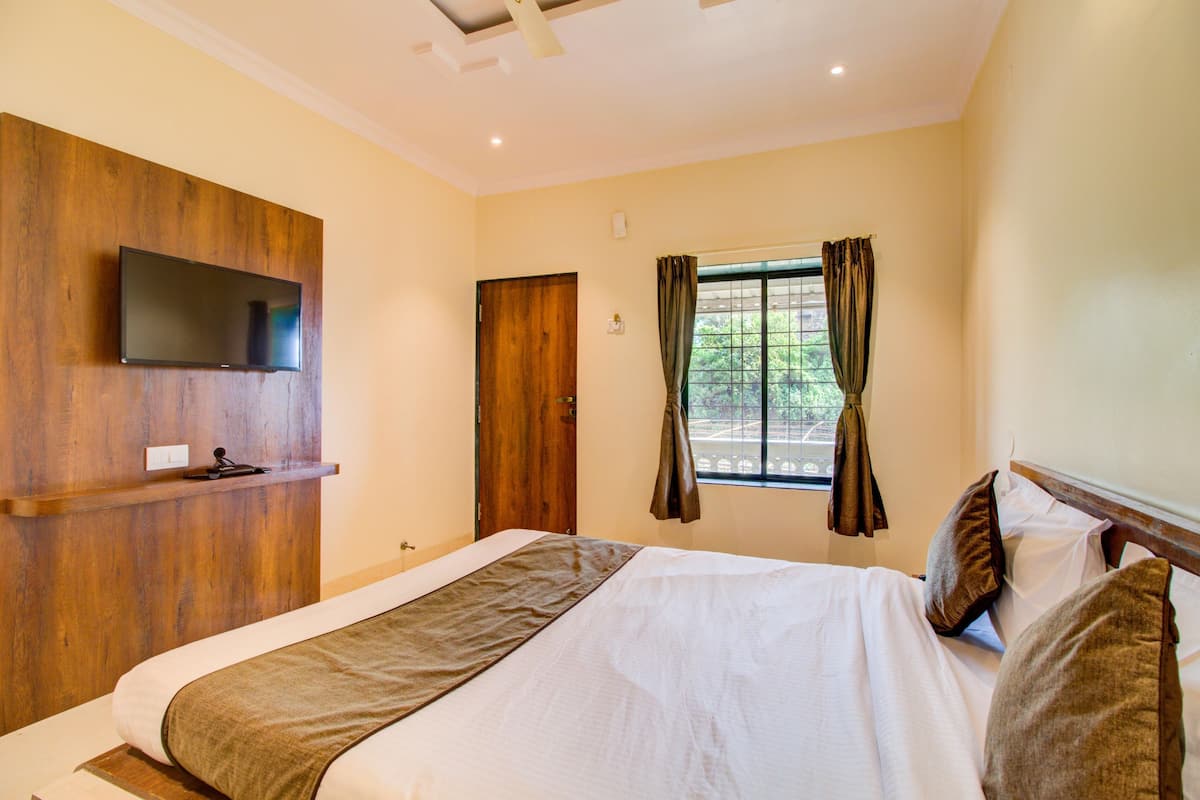 Una habitación de hotel con cama, televisor montado, ventana con cortinas y puerta.